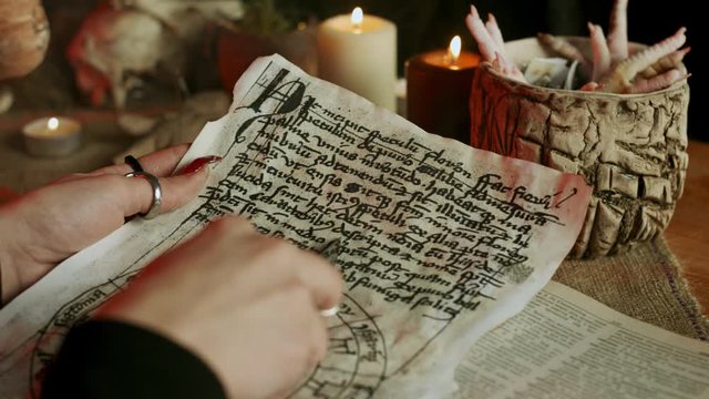 Partial view of witch with knife reading magic book page with spell