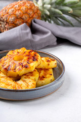 Heap of grilled pineapple slices on gray plate on concrete background.