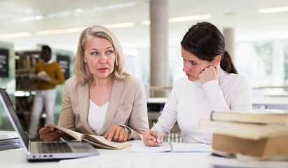 Female teacher working with girl student in university library