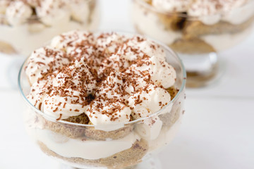 Tiramisu cake in glass, classic Italian dessert made of cookies savoiardi, mascarpone cream and cocoa. Coffee and diary dessert, homemade. selective focus. close up view