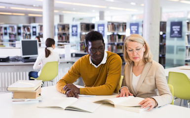 Two adult students studying together in public library
