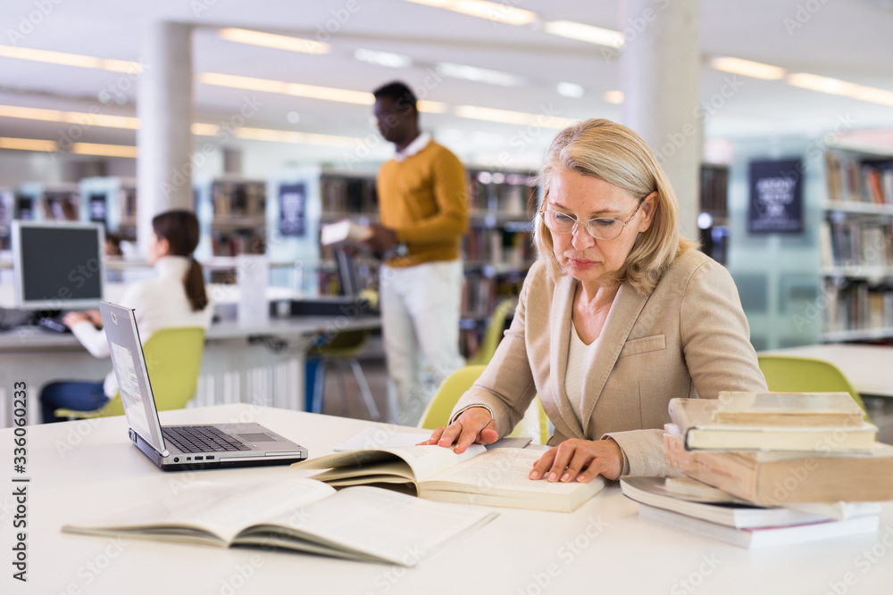 Canvas Prints Mature confident woman with laptop and book in public library