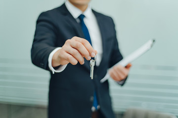 Real estate agent holding keys and contract agreement. In office. Concept for real estate, sale, moving home, renting property. Selective focus