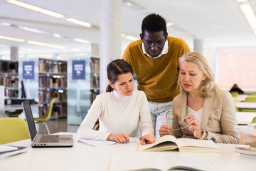 Students sitting in library, working with professor