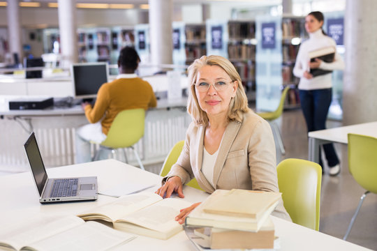 Portrait Of Positive Mature Woman With Book In Public Library