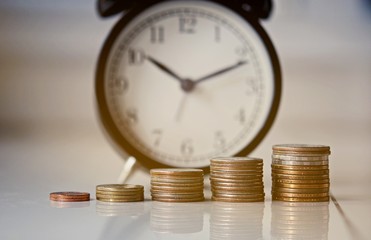 group of growing coins placed on the floor with blurred vintage alarm clock, selective focus and shallow depth of field, investment concept. growing on coin, Business Finance and Save Money.