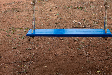 The wooden blue swings hung with rope in a spiral knot in the garden ground, No people.
