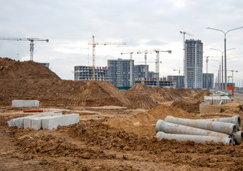 Fototapeta premium Drainage pipes at the large scale construction site against tower cranes. Installation of water main, sanitary sewer, storm drain systems. Renovation program, buildings industry background
