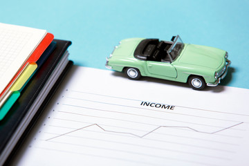 Miniature car model, diary, pen, graph with the word "Income"
