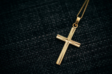 goldene Kette mit Kreuz-Anhänger vor schwarzem Grund
