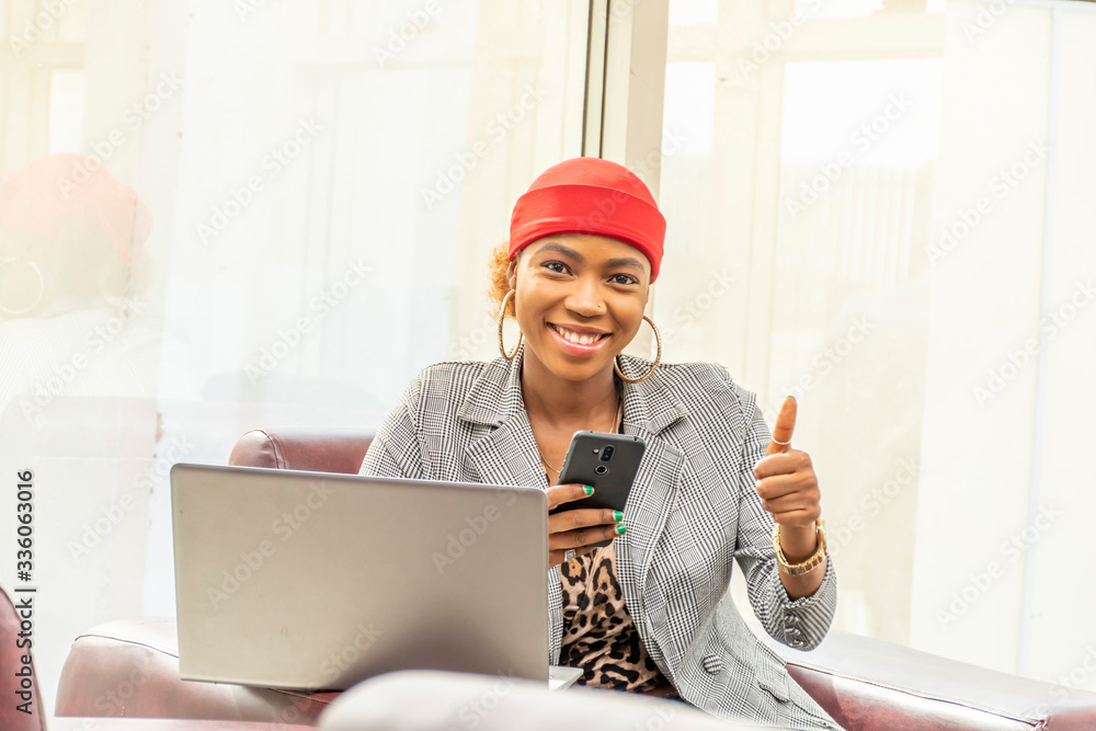 Wall mural beautiful young african muslim business woman using her laptop computer and smartphone smiling and g