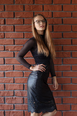 Elegant smiling woman in eyeglasses on a brick wall background