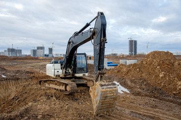 Excavator at earthworks on construction site. Backhoe loader digs a pit for the construction of the foundation. Digging trench for laying sewer pipes drainage in ground. Earth-Moving Heavy Equipment