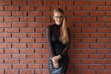 Elegant smiling woman in eyeglasses on a brick wall background