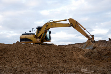 Fototapeta na wymiar Excavator at earthworks on construction site. Backhoe loader digs a pit for the construction of the foundation. Digging trench for laying sewer pipes drainage in ground. Earth-Moving Heavy Equipment