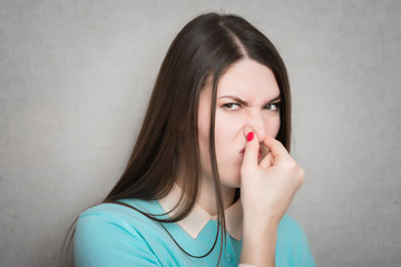 Young woman closes her nose with hand, isolated on grey