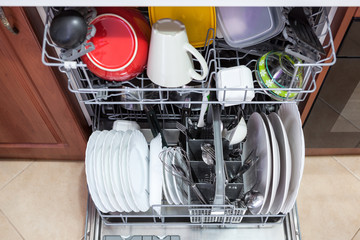 Opened dishwasher machine with clean utensil, steel spoons and cups is in the kitchen, top view