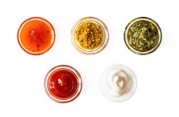 Sweet chili sauce, french mustard, basil pesto, ketchup and mayonnaise in glass bowls isolated on white background, top view. Various seasoning and dip border