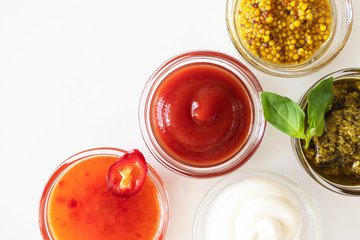 Ketchup, sweet chili sauce, pesto, french mustard and mayonnaise in glass bowls on a white background, top view. Various seasoning and dip