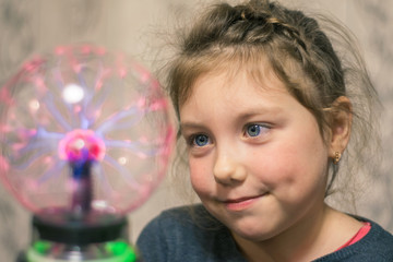 The child looks at the plasma ball. Portrait of a little girl with a magic ball. Kid plays witchcraft and magic.