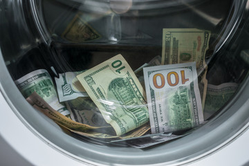 A lot of cash dollars is washed in the drum of a washing machine. Many banknotes are inside Washer. The concept of not legal money-laundering