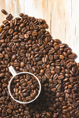 Roasted coffee beans with cup and wood background