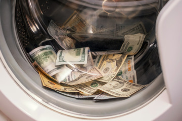 A lot of cash dollars is washed in the drum of a washing machine. Many banknotes are inside Washer. The concept of not legal money-laundering