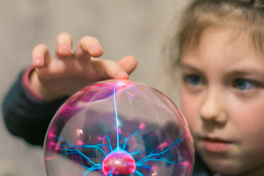 The child touches the plasma ball with his finger. Selective focus.