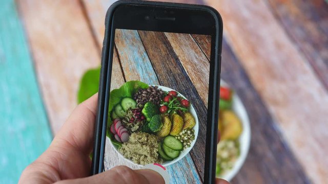 Man Hand Takes Photo Of Food On Table With Cell Phone. Healthy Vegan Food. Smartphone Photo For Social Networks Post. 