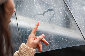 girl is painting the heart on a foggy surface in the rain under an umbrella. Love story concept