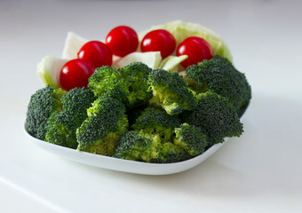 Healthy lifestyle concept: Vegetables (cabbage, tomato, broccoli) on a white plate on a white table