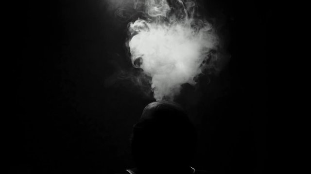 the silhouette of a man on a dark background exhales clouds of smoke