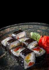 sushi roll with salmon, cucumber, cream cheese, rice in plate on black wooden table background