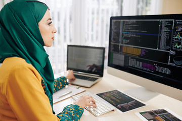 Young muslim coder using computer and laptop when testing new program whe wrote