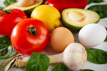 fresh tomatoes, avocado, red sweet pepper, lemon, spinach, eggs, onion, garlic on a white ,  healthy food
