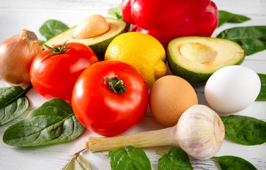 tomatoes, avocado, red sweet pepper, lemon, spinach, eggs, onion, garlic on a white background,  healthy food