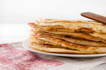 stack of round Russian pancakes on a plate, kitchen spatula on a towel with a red pattern on a white , side view