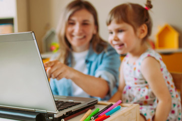 Fototapeta premium Smiling mother and toddler daughter looking at the notebook indoor