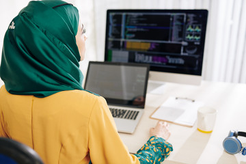 Young female muslim code in beautiful emerald hijab working on computer at her office desk