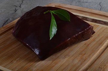 A piece of fresh beef liver on a wooden kitchen board and decorated with green bay leaves
