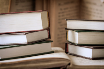 Two stack of hard back books against the background of other open books. Selective focus. Education, school, study, reading concepts