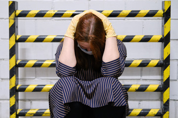 Girl in a medical mask holds her head against the background of a fire barrier with yellow-black...
