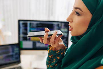 Beautiful muslim female software engineer recording voice message for coworker