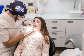 Young bearded male dentist drilling tooth to female patient