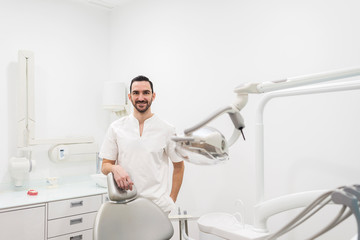 Portrait of a handsome dentist wearing a white uniform, standing in a dentist clinic.