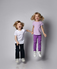 Two happy laughing kids boy and girl in casual stylish clothes jump together having fun