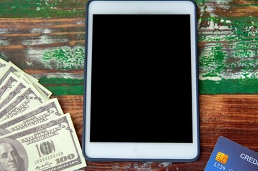 Dollar bills, credit card and digital devices tablet with technology and money on a wooden background