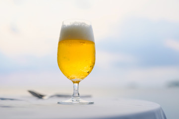 Mug of cold beer with foam on the table. Against the background of the sea in Restaurant