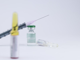 Defocused ampoule with another fallen on white surface and an injection placed on a vial showing...