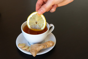 
Cup of tea with lemon and ginger in hands close-up on a black background. Alternative medicine to...